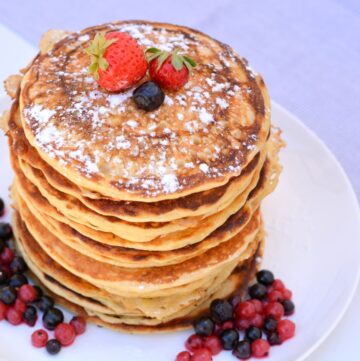 Stapel versgebakken American Pancakes met zuurdesem op een wit bord gedecoreerd met rood fruit