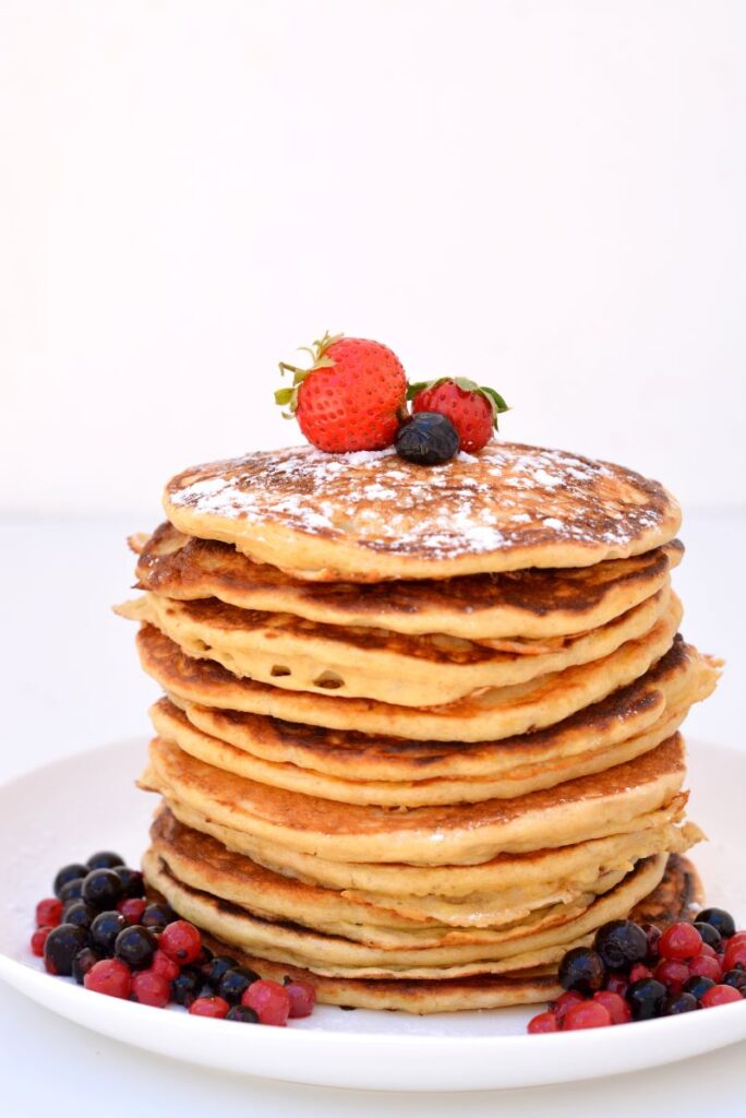 Stapel American pancakes met zuurdesem op een wit bord gedecoreerd met aardbeien en bosbessen.