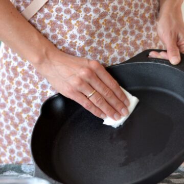 Vrouw gaat gietijzeren pan inbranden en smeert met een stuk keukenrol gesmolten kokosolie op de verwarmde pan