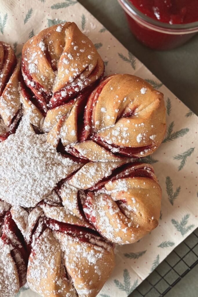 Versgebakken kerst sterbrood met cranberry jam ligt op een gedekte kersttafel bestrooid met poedersuiker.