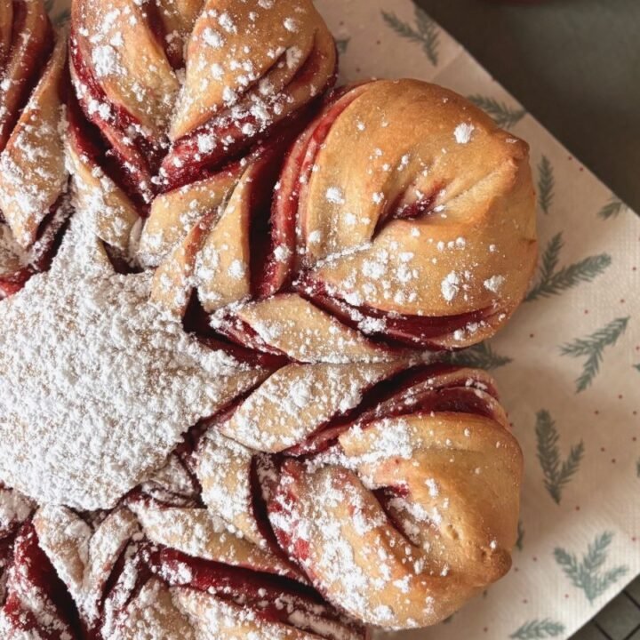 Versgebakken zuurdesem cranberry ster brood ligt op bakkpapier op de tafel naast een pot eigengemaakte cranberry jam