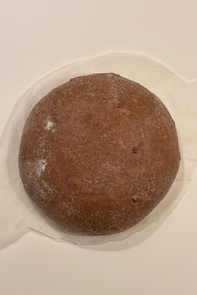 Chocolade zuurdesem deeg in een boule ligt op bakpapier op een wit tafelblad