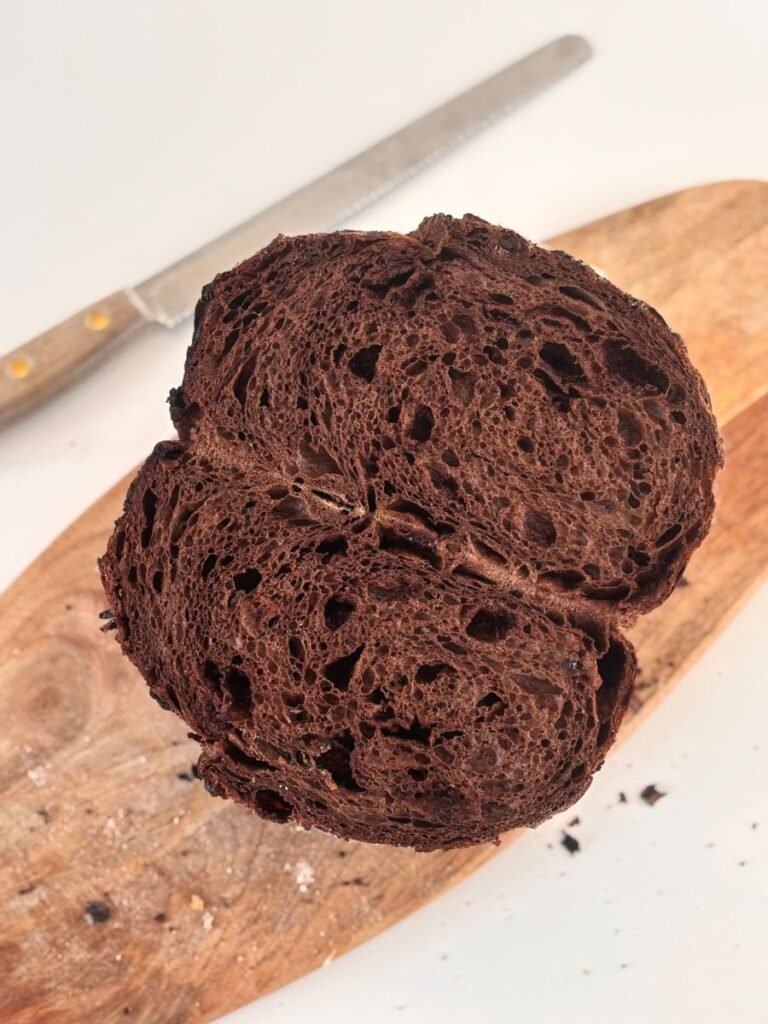 Een versgebakken chocolade zuurdesem brood ligt doorgesneden en open op een houten plank. 