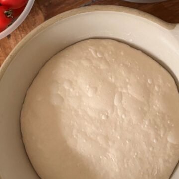 Gerezen deeg met luchtbellen ligt in een beige stenen kom op een houten tafelblad.
