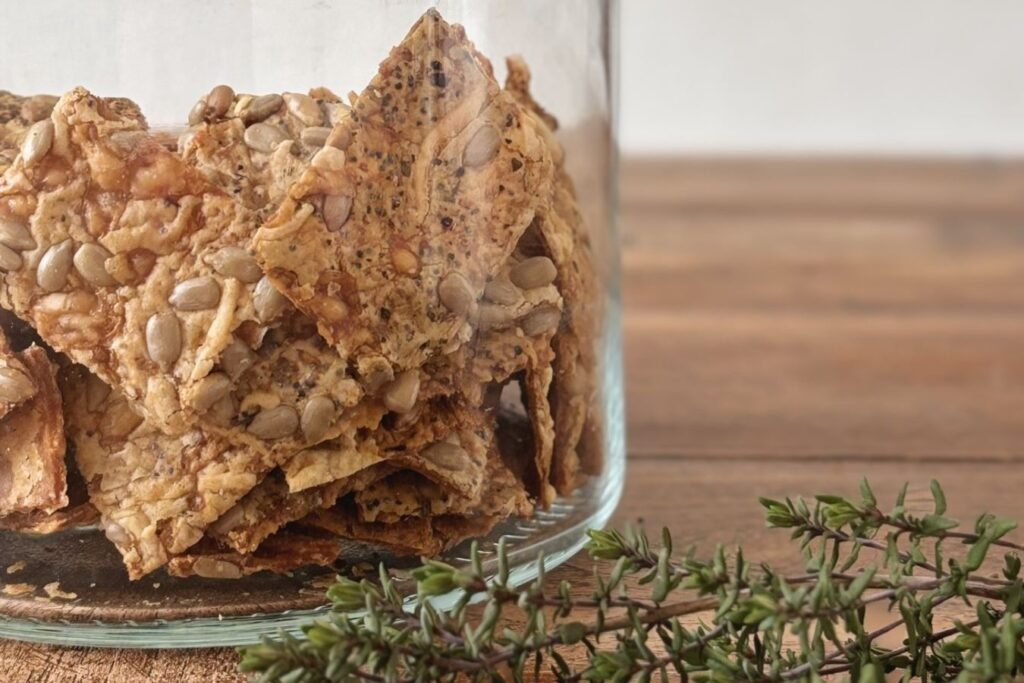 Knapperige versgebakken zuurdesem crackers met zonnebloempitten, kaas en verse kruiden staan in een glazen pot op een houten eettafel