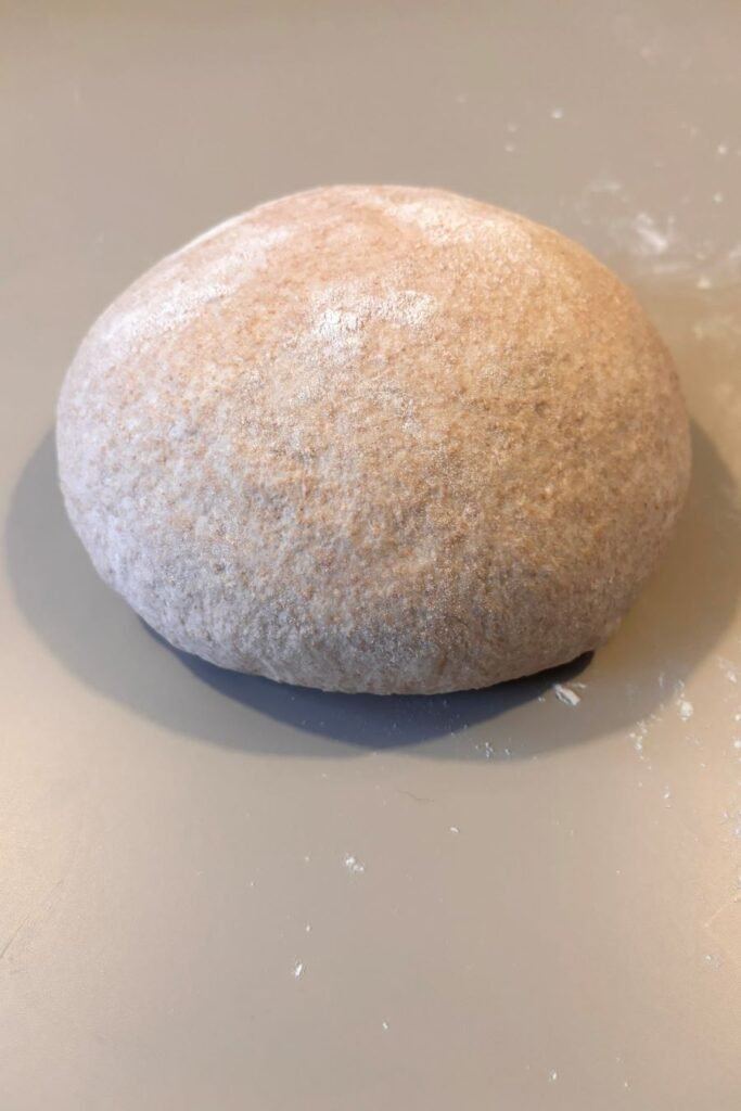 Gerezen zuurdesem deeg ligt in een boule gevouwen op wit tafelblad