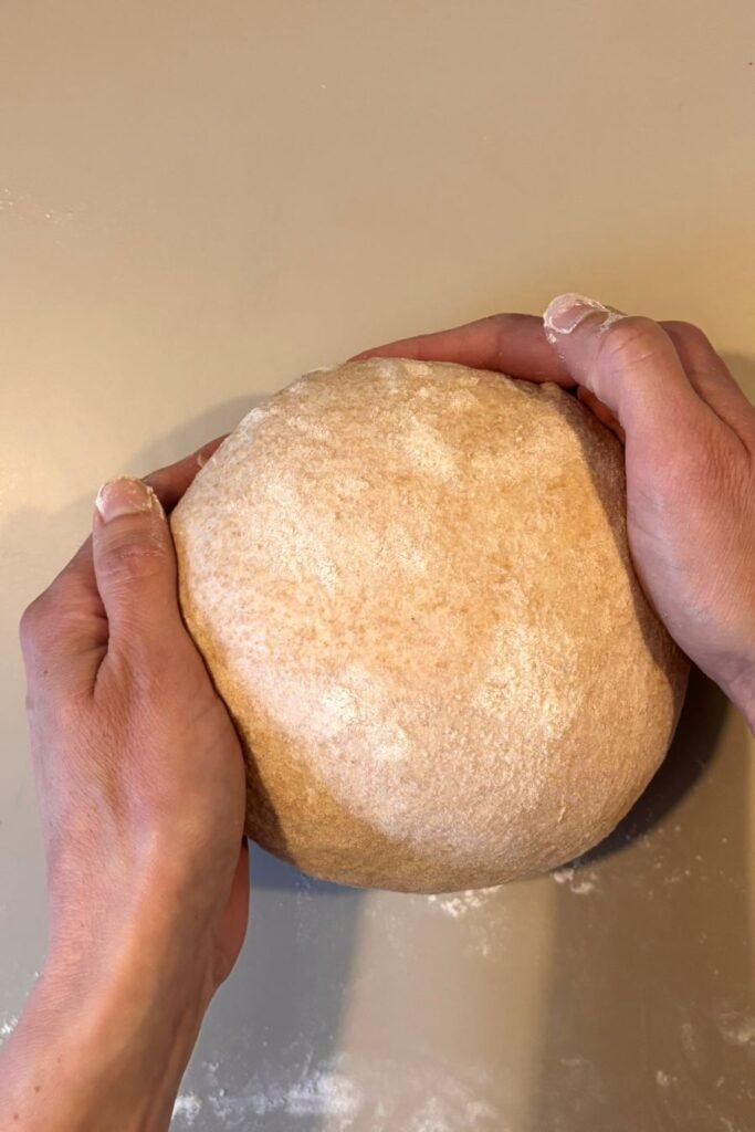 Vrouw gaat zuurdesem brood maken en vouwt het gerezen deeg op een tafelblad tot een mooie boule