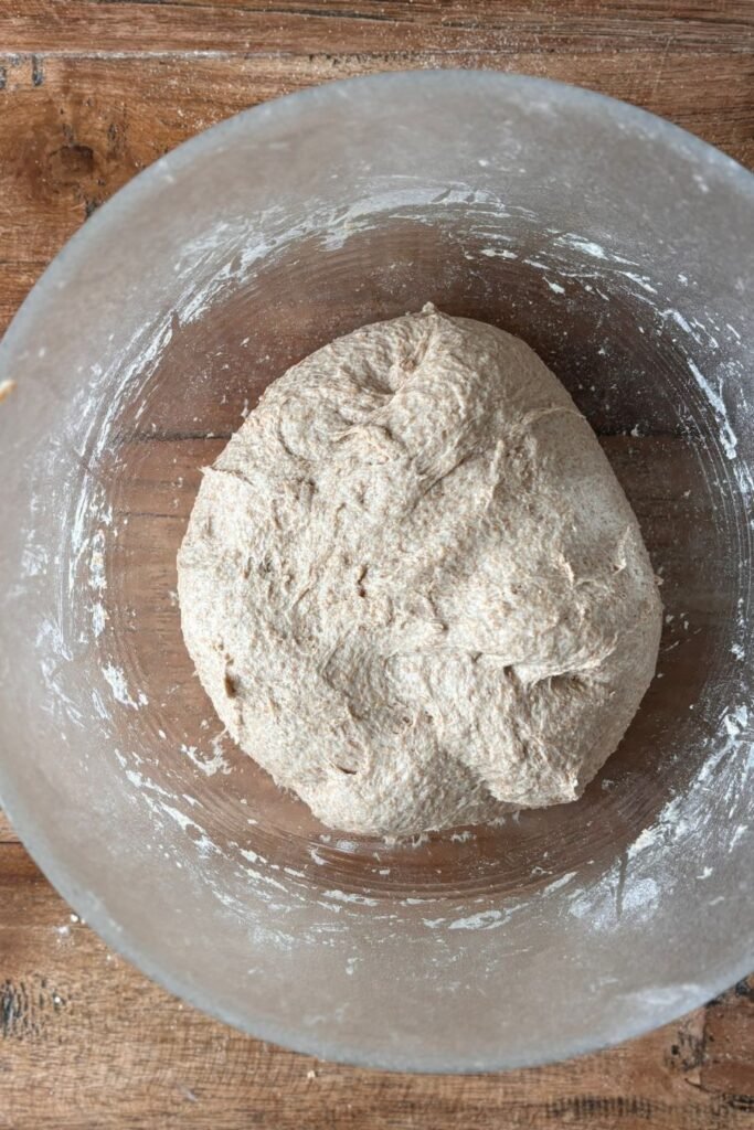 Deeg voor volkoren zuurdesem brood ligt in een glazen schaal op houten tafelblad