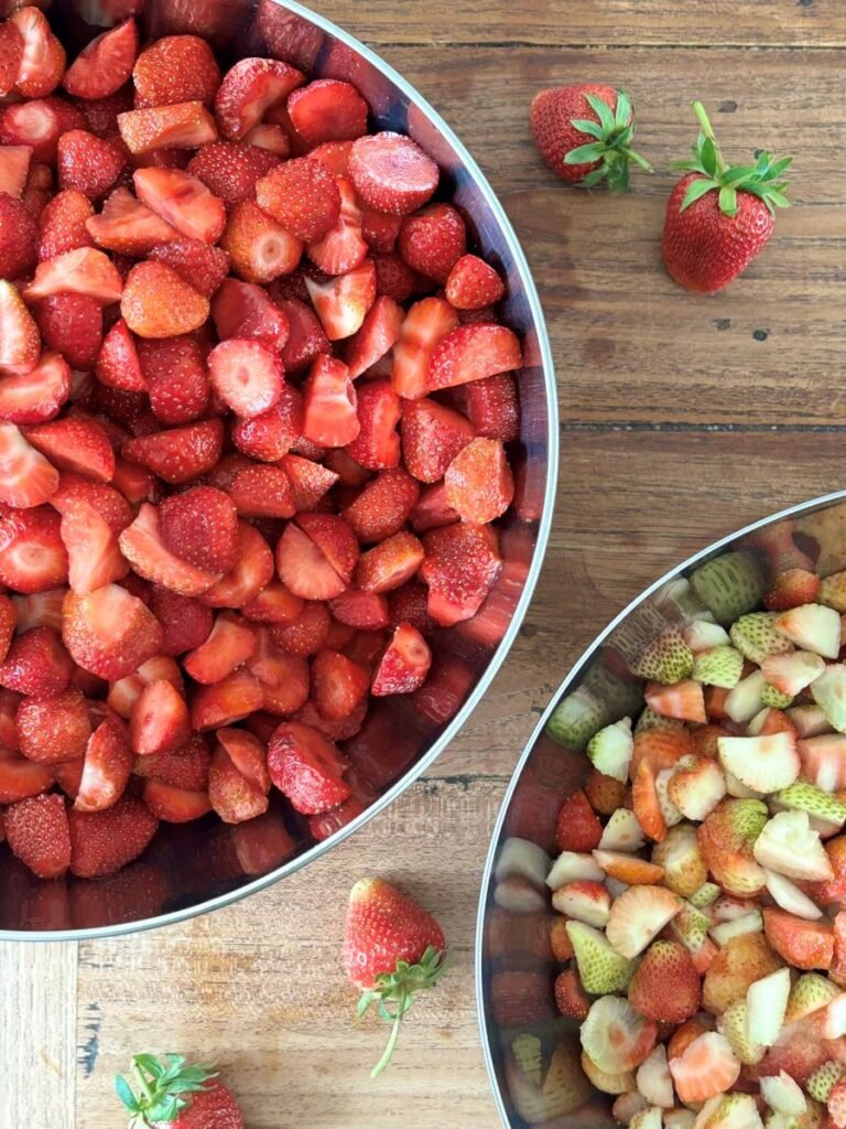 Gesneden aardbeien liggen in 2 grote bakken, klaar om jam mee te maken.