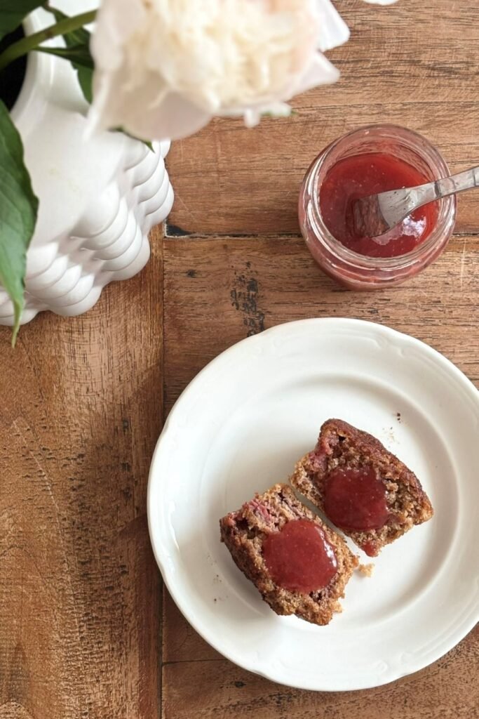 Doorgesneden muffin van volkoren speltmeel met een klodder aardbeienjam ligt op een schoteltje op tafel
