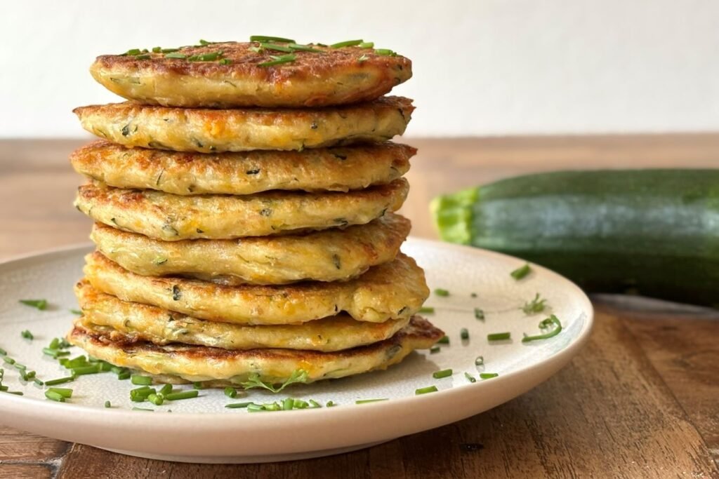 Versgebakken stapel courgette pannekoeken ligt op een stapel op een bordje, bestrooid met versgeknipte bieslook