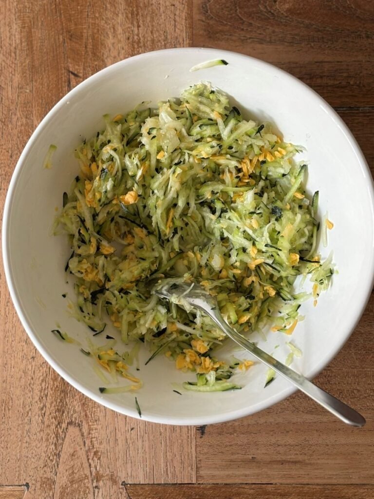 Geraspte kaas wordt in een schaal door geraspte courgette en geraspte ui gemengd