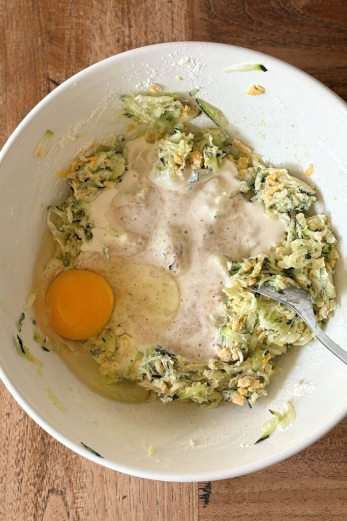 ei en zuurdesem discard zijn toegevoegd aan schaal met geraspte courgette, ui en cheddar kaas