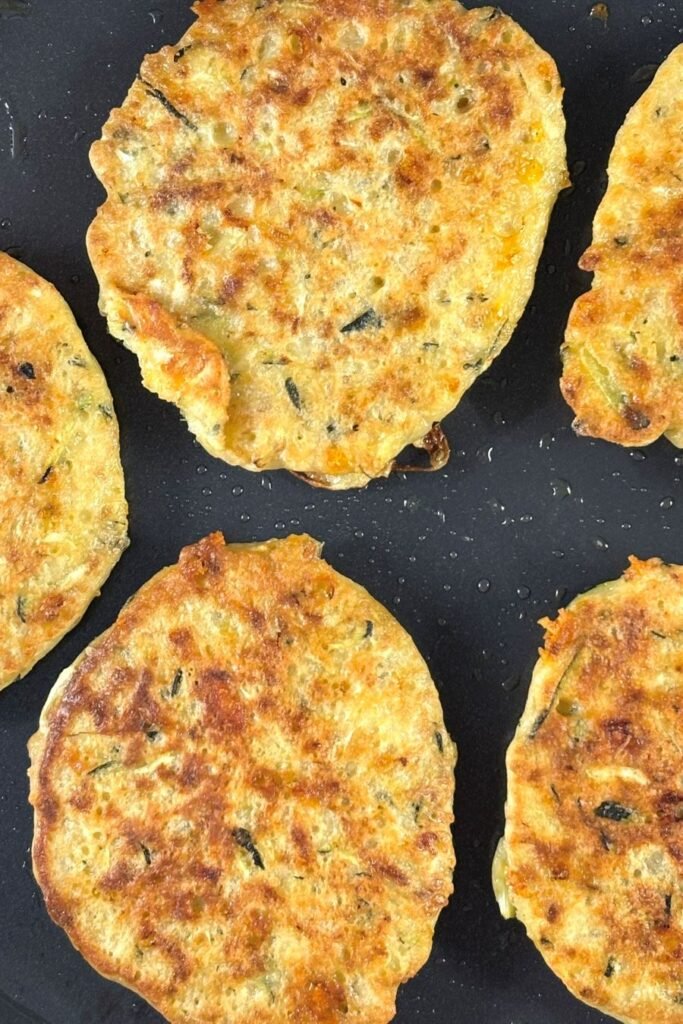 Krokante courgette pannekoeken liggen in een koekenpan te bakken
