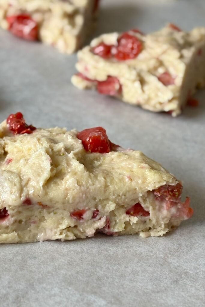 Zuurdesem scones met stukjes aardbei liggen klaar op bakpapier om afgebakken te worden.
