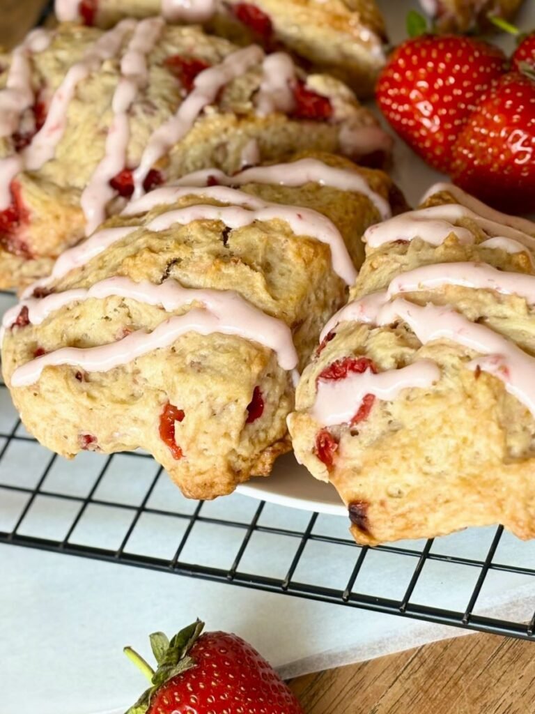 Versgebakken aardbeien scones met aardbeien icing liggen op afkoelrooster af te koelen. 