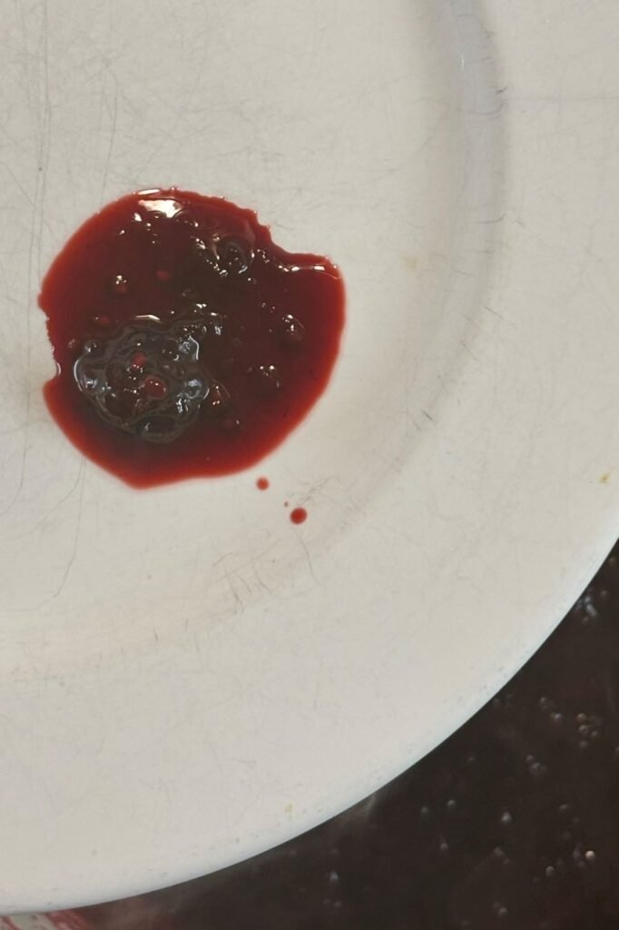 Een klodder hete bramenjam ligt op een bordje uit de vriezer om te kijken of de jam genoeg stolt. 