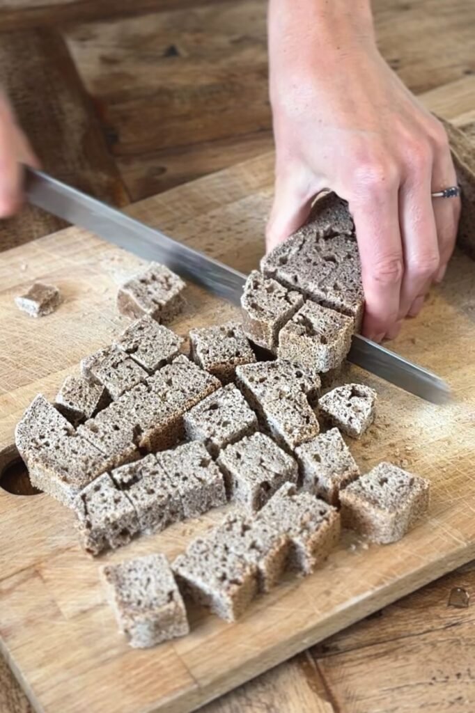 Vrouw gaat broodkruim maken en snijd oud brood in groffe stukken op een houten snijplank