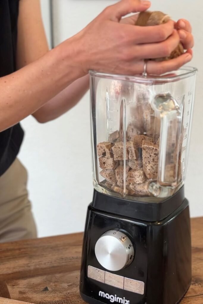 Vrouw gaat broodkruim maken en stopt oude stukken brood in een Magimix blender