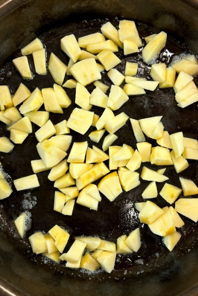 Stukjes appel worden in een gietijzeren pan gebakken in roomboter