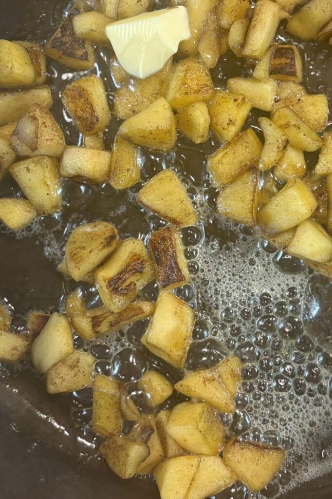 Gebakken stukjes appel met kaneel liggen in gesmolten roomboter in een gietijzeren pan