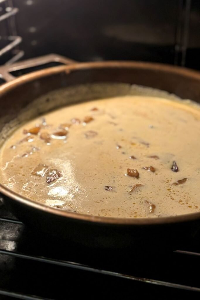 Een gietijzeren pan met stukjes appel en beslag voor een Dutch Baby pannenkoek staat in de oven te bakken