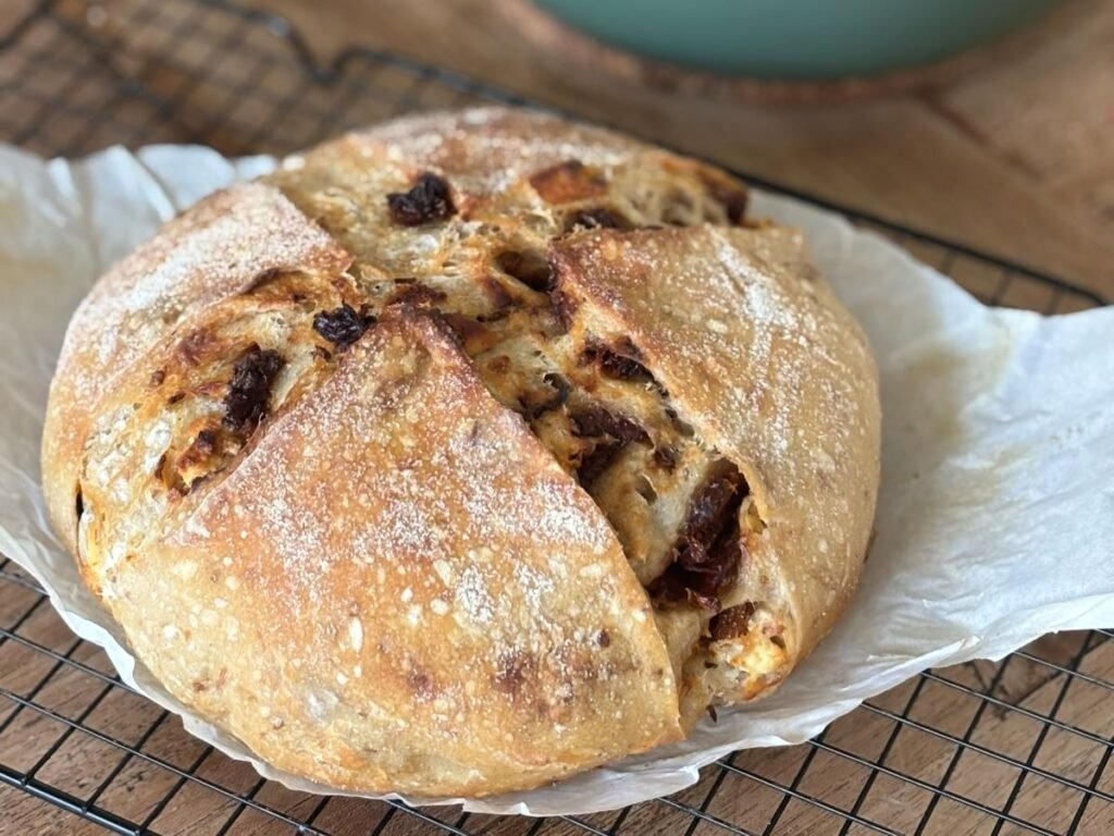 Versgebakken Italiaans zuurdesembrood met zongedroogde tomaatjes en geitenkaas ligt op een rooster af te koelen