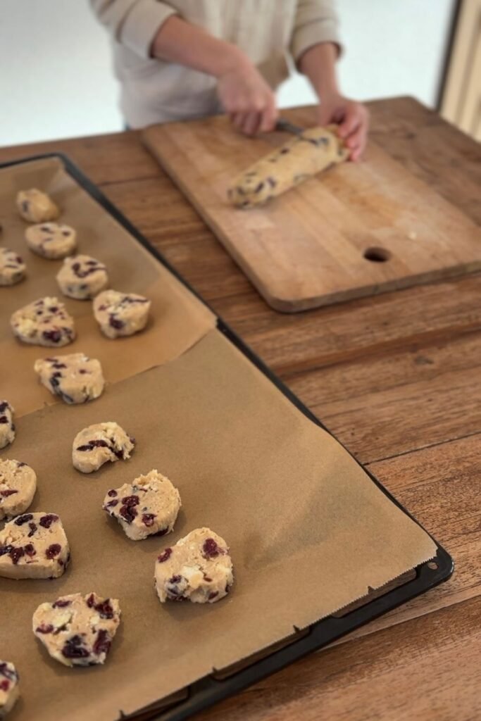 Deeg voor cranberry koeken met witte chocolade wordt gesneden en in schijfjes op een bakplaat met bakpapier gelegd