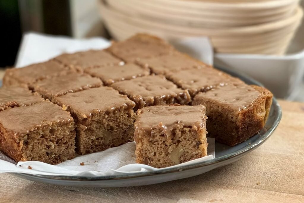 Versgebakken speculaas cake ligt in blokjes gesneden gepresenteerd op een bord met op de achtergrond zuurdesem banneton mandjes