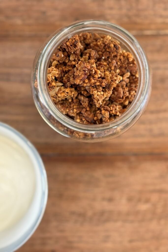 Glazen pot met zelfgemaakte crunchy muesli staat op een houten tafelblad.