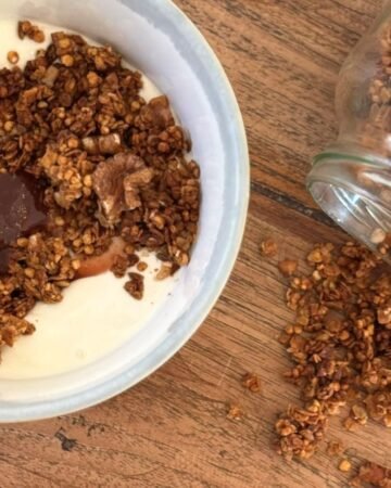 Versgebakken cruesli ligt op keukenblad naast een kom met griekse yoghurt en aardbeien jam