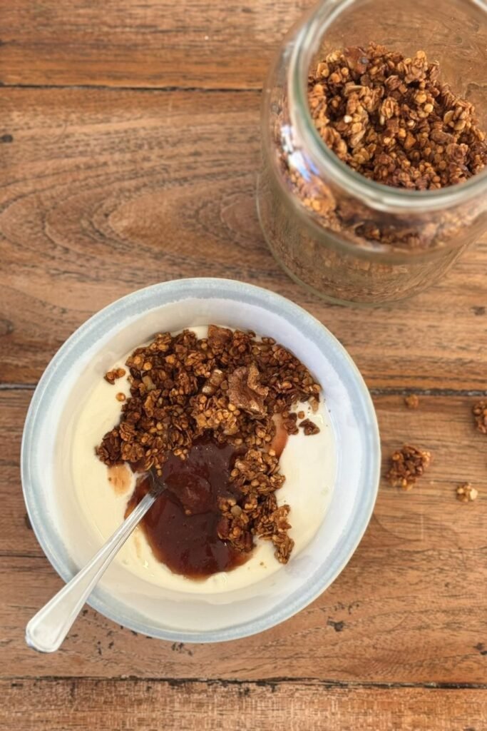 Zelfgemaakte cruesli met Griekse yoghurt en aardbeien jam ligt in blauwe kom op een houten eettafel