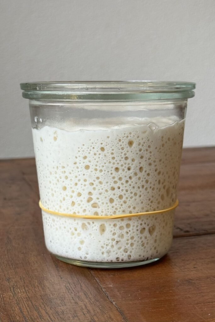 Actieve zuurdesem starter met veel luchtbellen staat in een weckglas op een houten eettafel