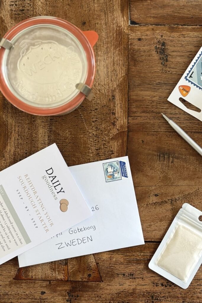 Iemand wil zuurdesem starter kopen dus op de eettafel ligt een gedroogde zuurdesem starter in een zakje naast een envelop waarin de starter gepost wordt