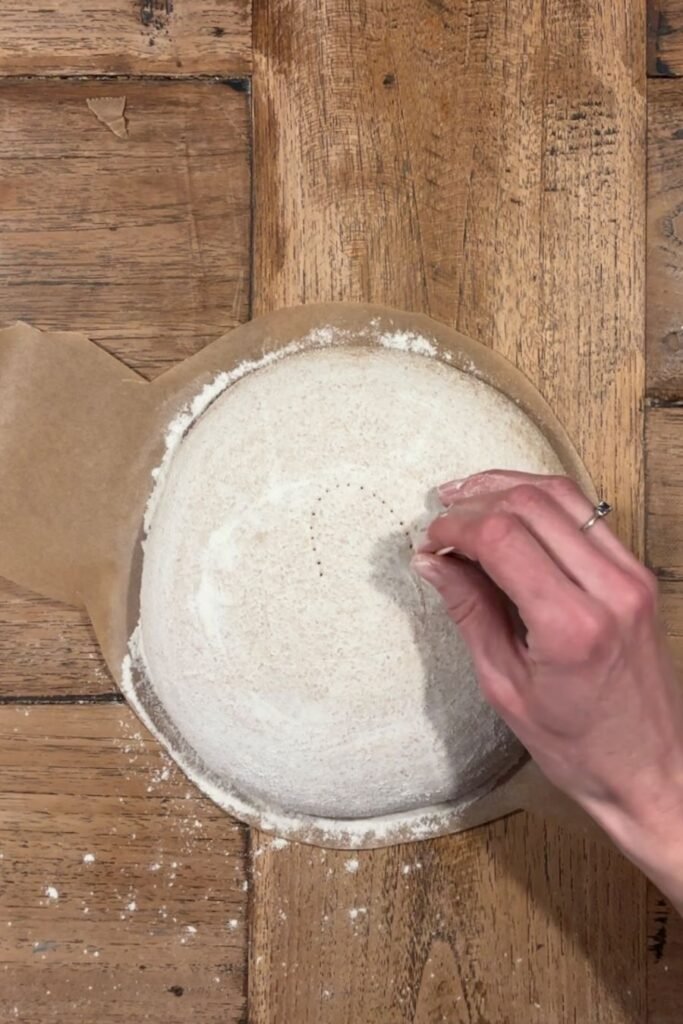 Vrouw prikt met een sateprikker in rond zuurdesem deeg om een mooi hart te maken