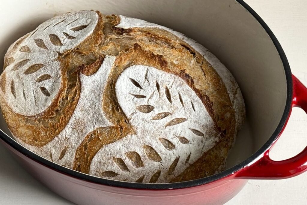 Zuurdesem volkoren brood ligt versgebakken in een gietijzeren pan. Het zuurdesembrood is mooi ingesneden met hart vormen