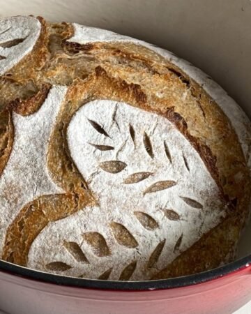 Zuurdesem volkoren brood ligt versgebakken in een gietijzeren pan. Het zuurdesembrood is mooi ingesneden met hart vormen