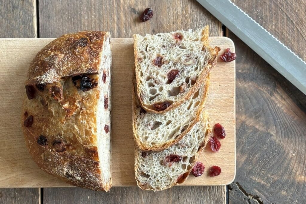 Versgebakken en gesneden zuurdesembrood met cranberry en walnoot ligt op een houten plank naast een broodmes