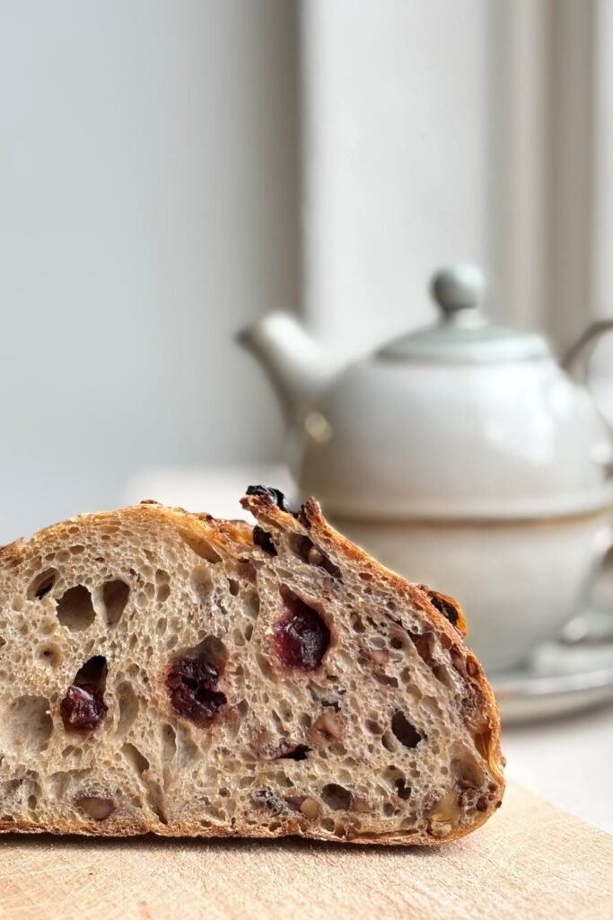 Versgebakken zuurdesem brood met cranberries en walnoten ligt op een houten plank voor een antieke theepot
